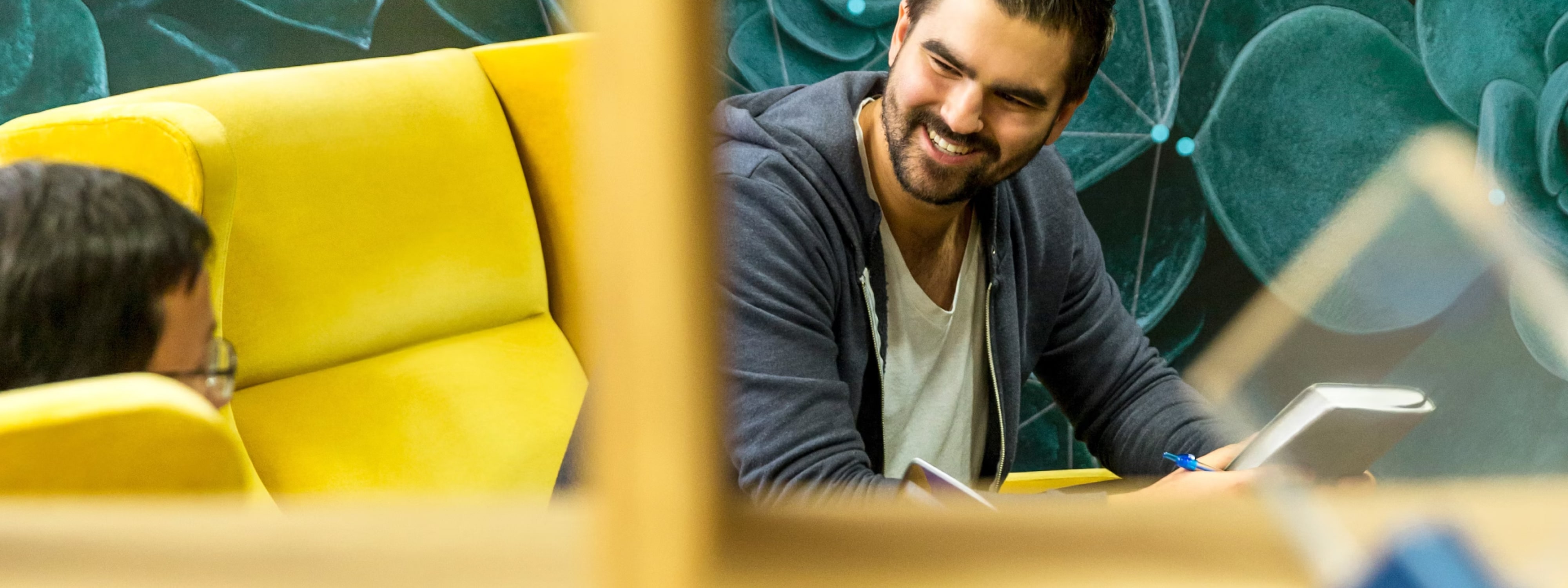 Smiling man leaning on table in a lounge with yellow and teal seating